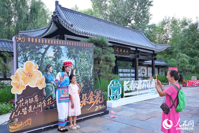 游客在长影经典作品《五朵金花》海报前，与NPC演员合影留念。人民网记者 李洋摄